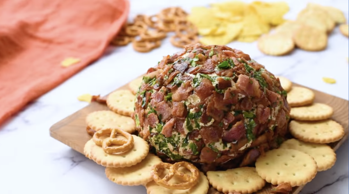 a bacon ranch cheese ball on a tray with crackers and pretzels.