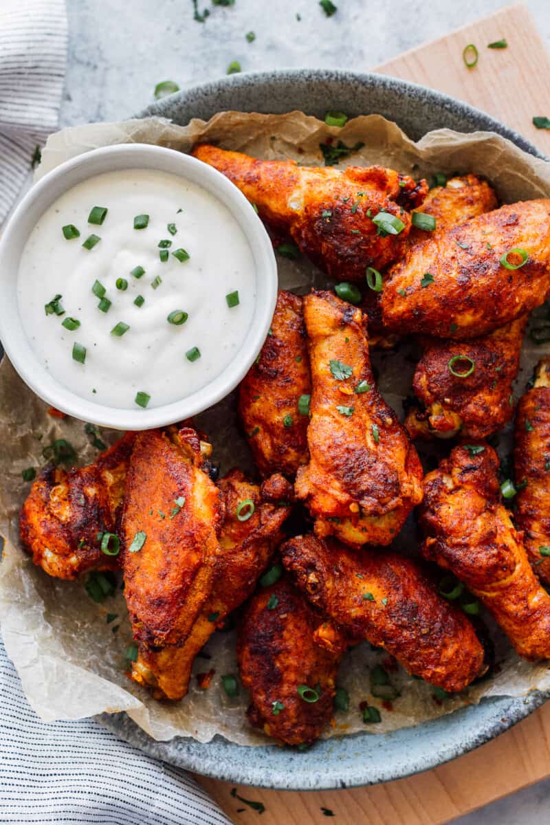Baked Chicken Wings have the most amazing Chicken Wing Seasoning consisting of paprika, garlic, salt and pepper. If you've wondered How to Bake Chicken Wings that are crispy, flavorful, and amazing, this recipe is for you! EASY Baked Chicken Wings do exist and they're just as delicious, and definitely healthier, when baked and not fried. This is our very favorite Baked Chicken Wings Recipe! simple spiced baked chicken wings on platter with ranch