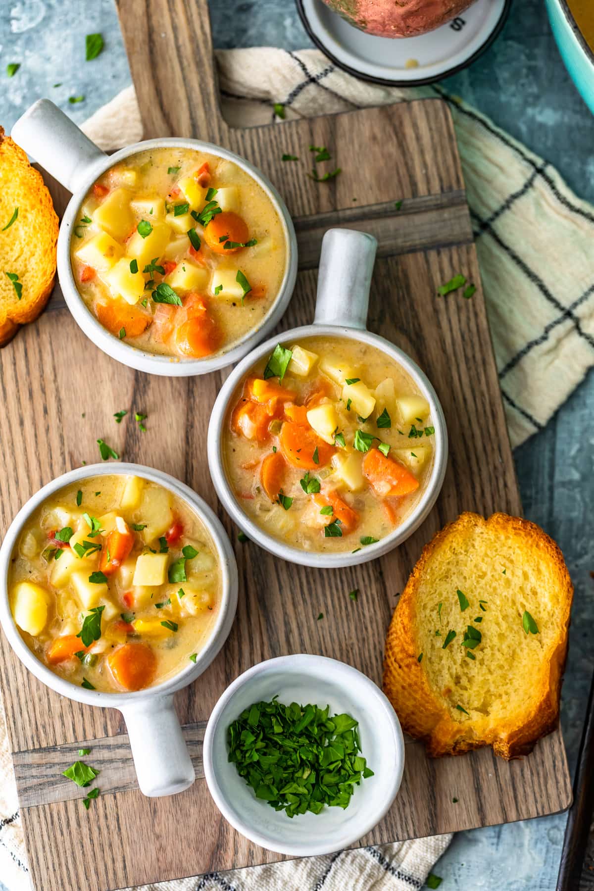 three bowls of potato chowder on a wood cutting board