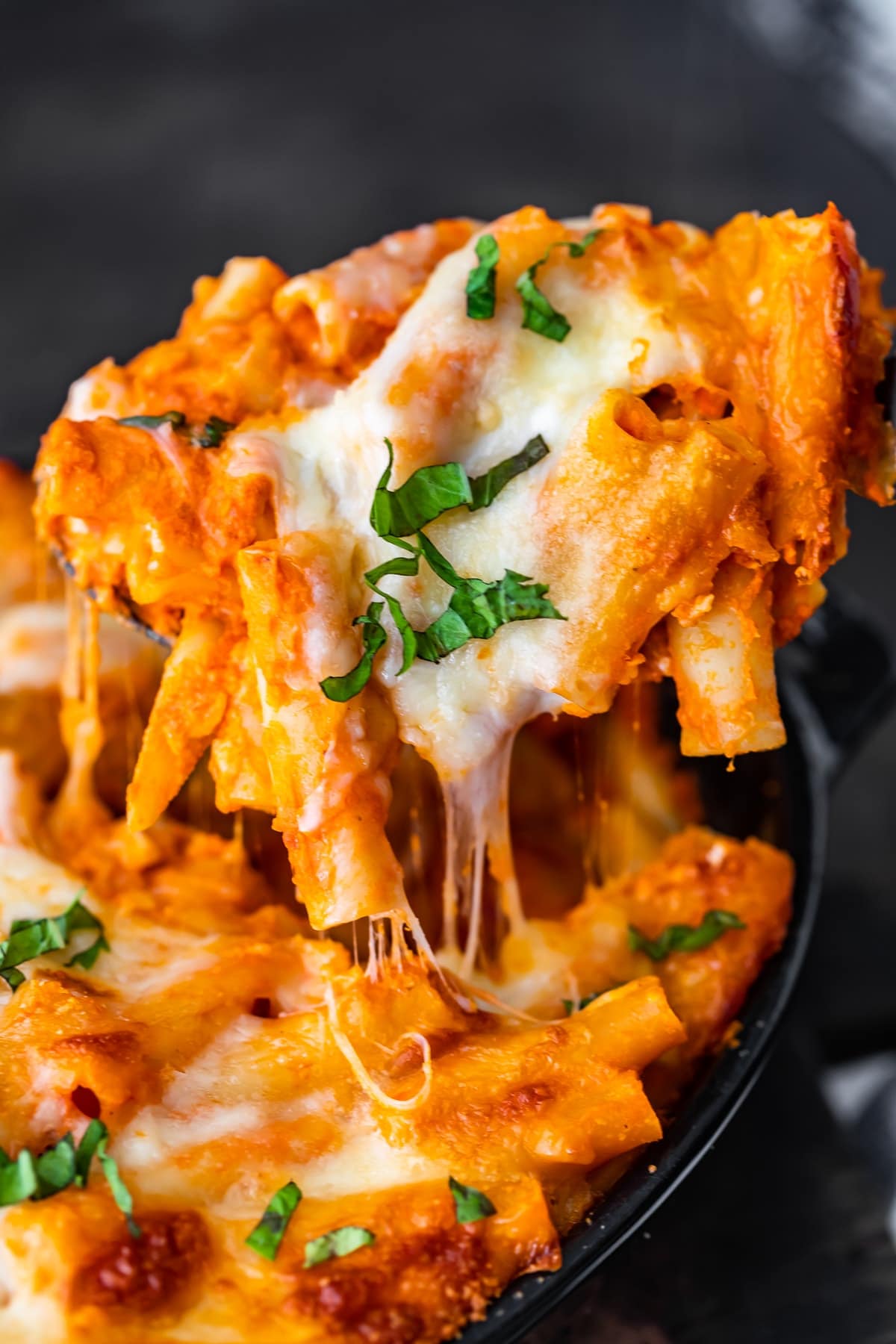 scooping a serving of cheesy baked ziti out of the casserole dish