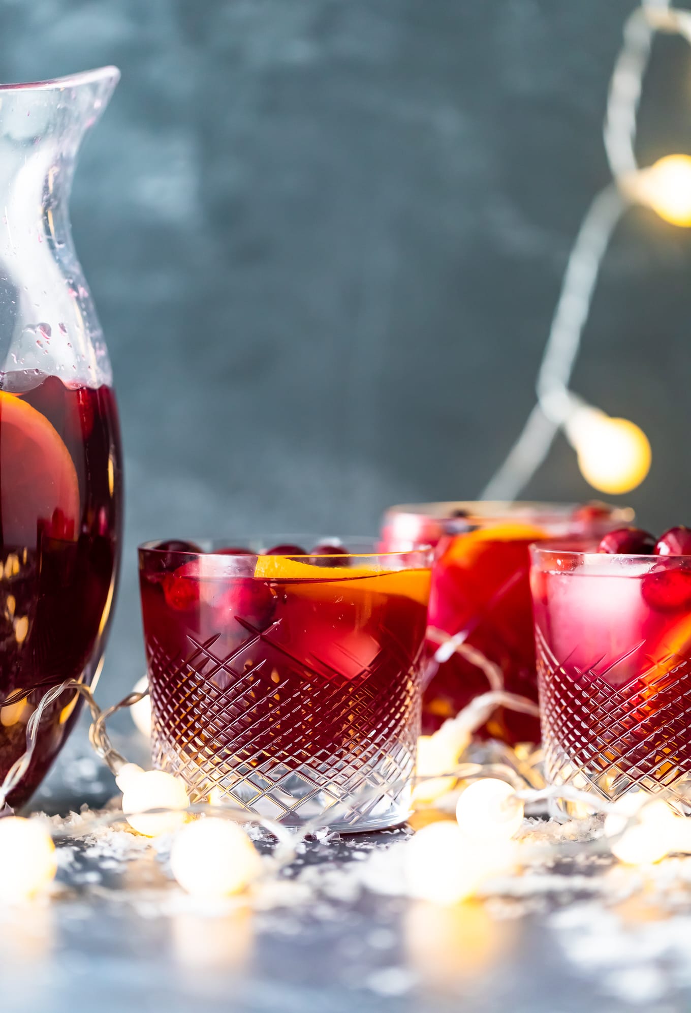 Orange Cranberry Sangria is fresh, fun, and festive. This Christmas Sangria recipe is just perfect for the holiday season! glasses of Christmas sangria with Christmas lights in the background