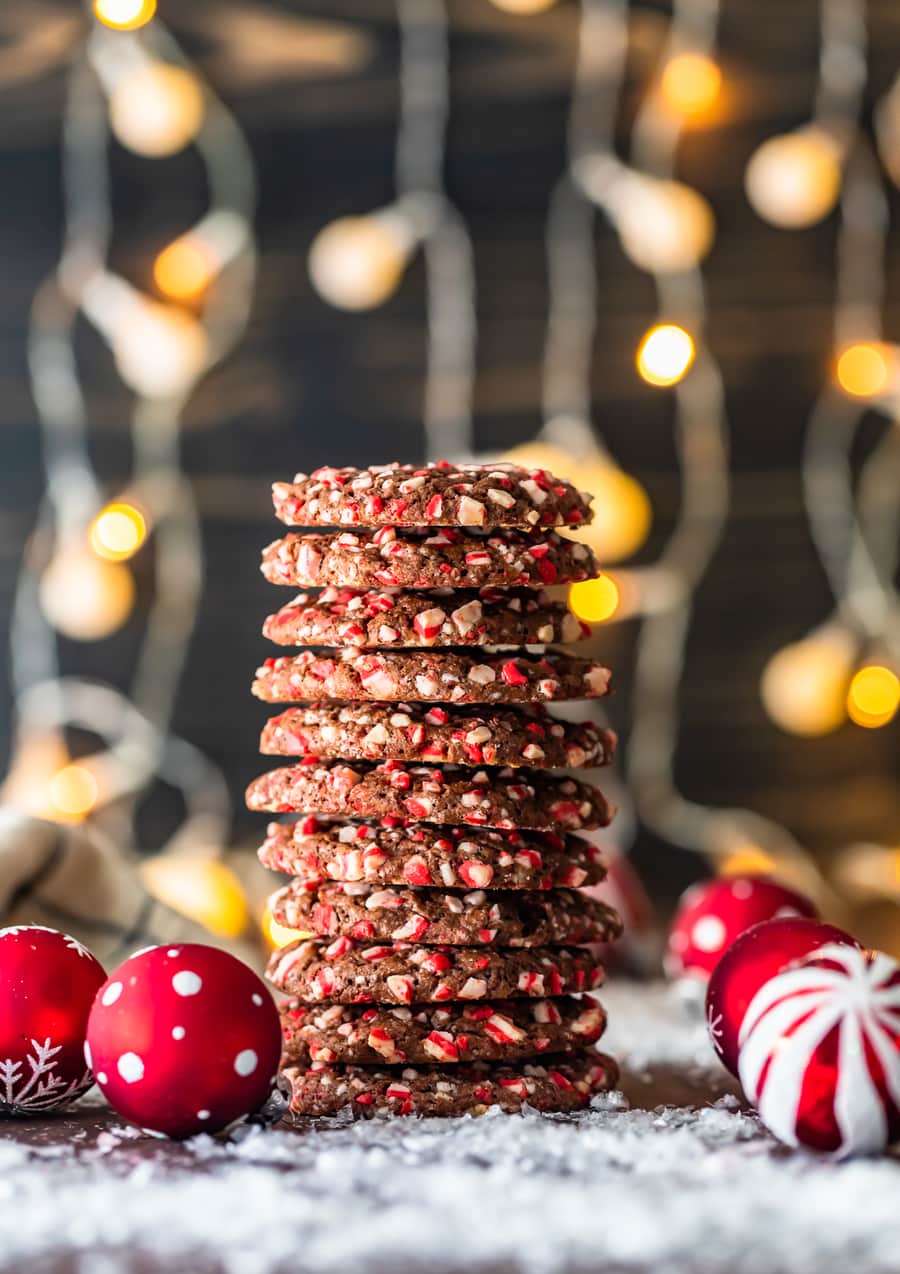 chocolate peppermint cookies stacked high, with christmas lights in the background and christmas ornaments in the foreground
