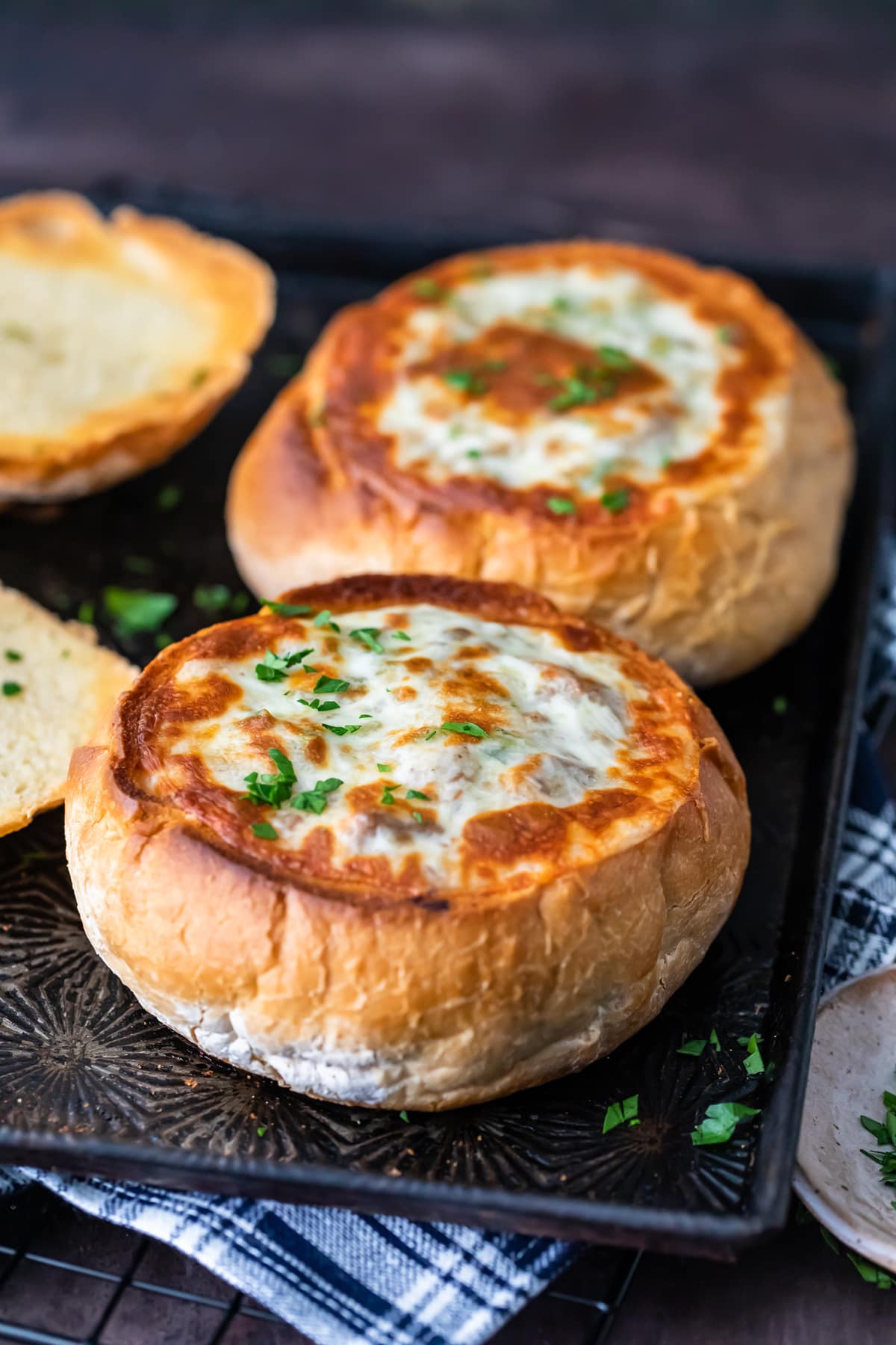 Bread bowls on a baking tray, filled with soup and topped with cheese