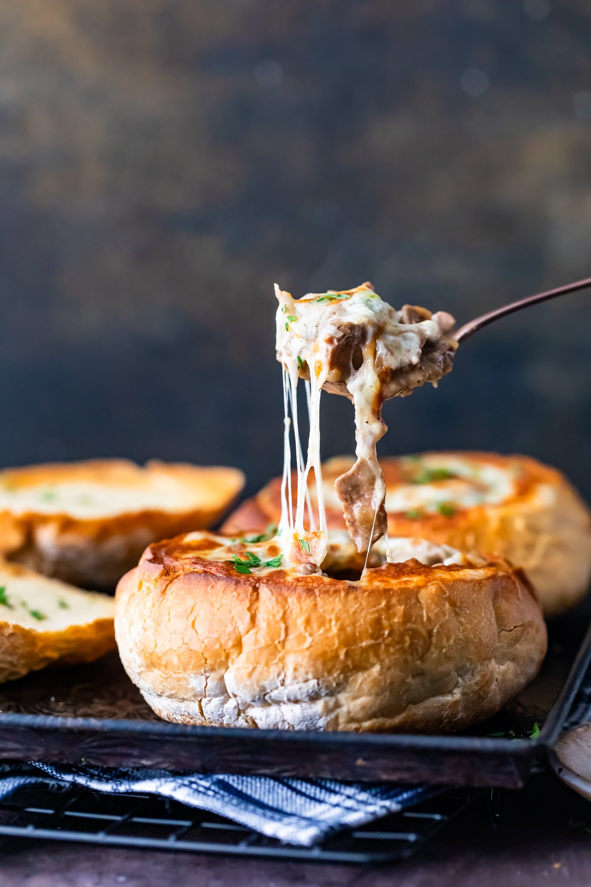side view of a bread bowl soup, pulling a spoonful of cheesy soup out of the bowl