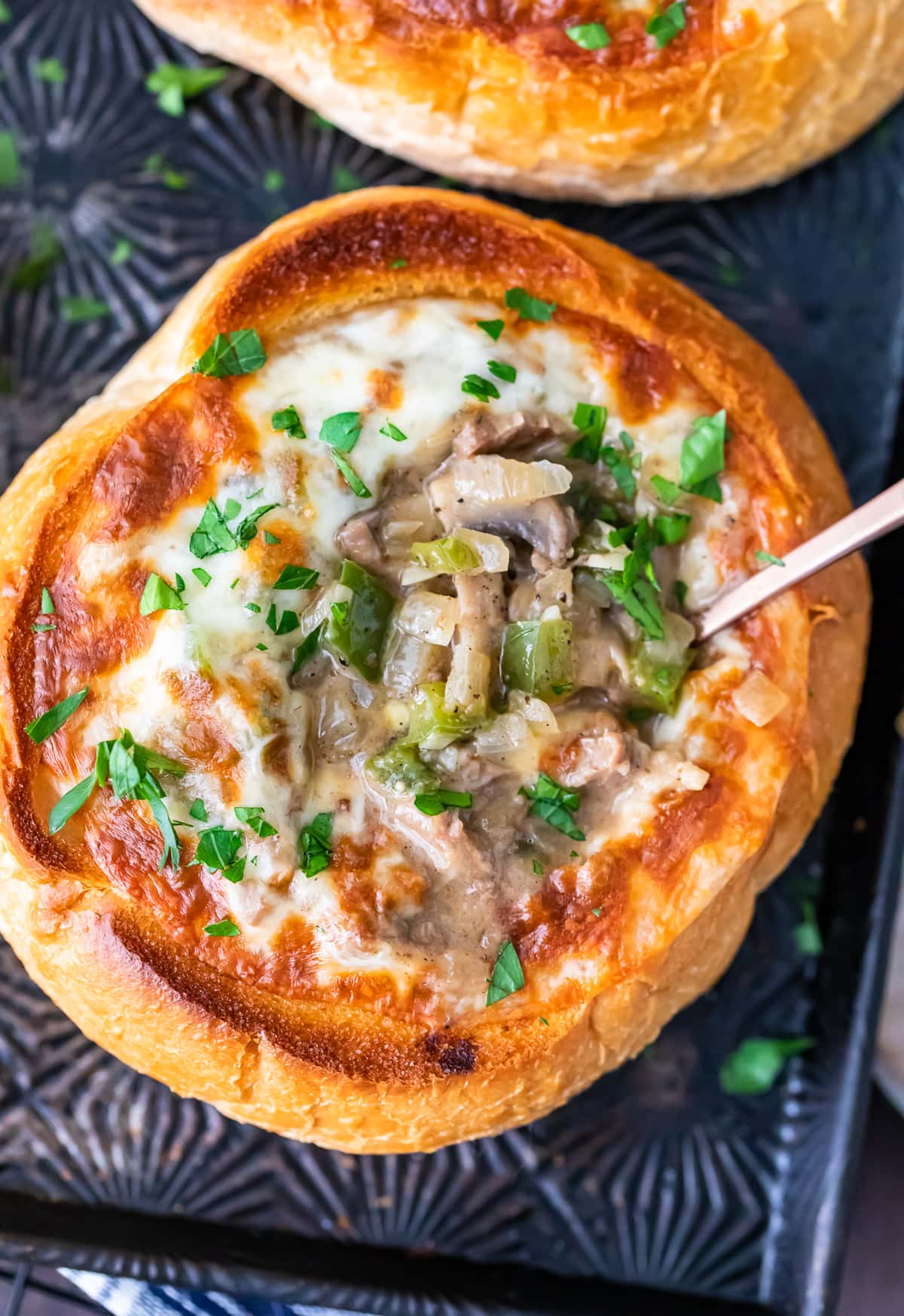 close up on a bread bowl soup filled with beef, cheese, onions, mushrooms, and green peppers