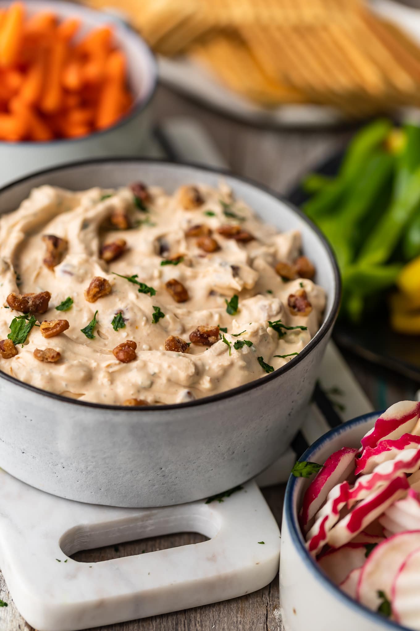 a bowl of blue cheese dip next to bowl of carrots, peppers, and radishes