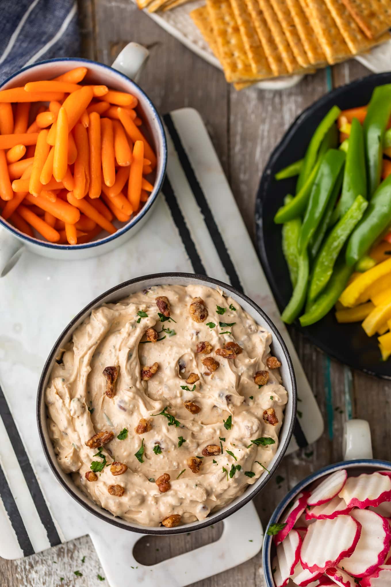 a bowl of veggie dip sitting on a cutting board, surrounded by bowls of veggies