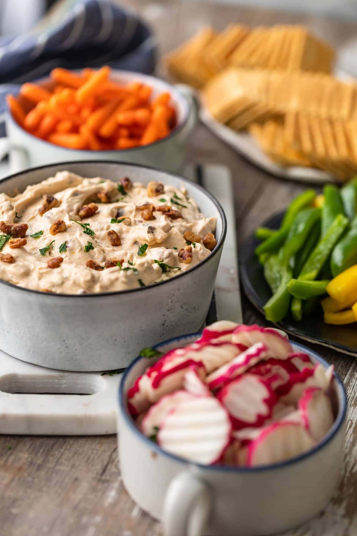 an array of bowls filled with veggies, crackers, and dips