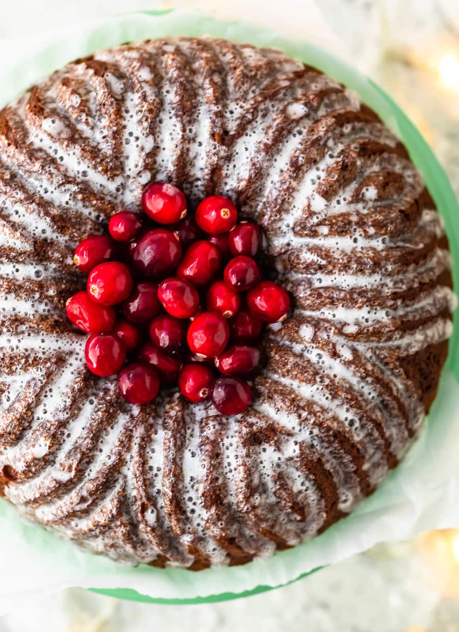 overhead view of a gingerbread bundt cake topped with cranberries and a lemon glaze