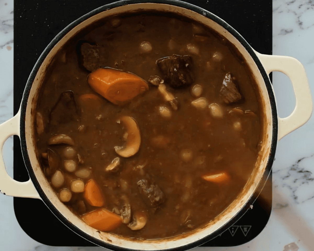 A pot of beef bourguignon with mushrooms, pearl onions, carrots, and tender beef pieces in a thick gravy.