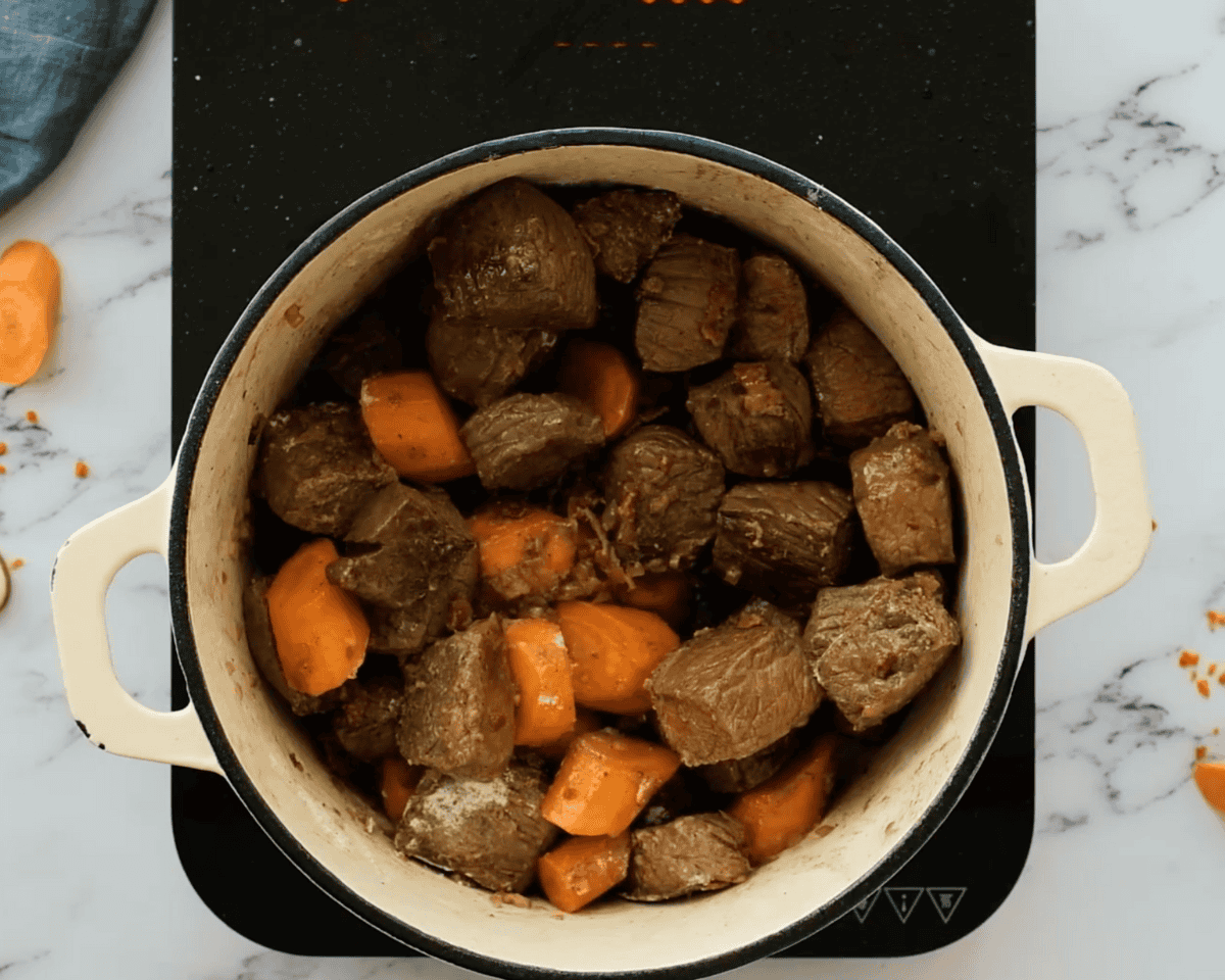 Seared beef cubes and browned carrots mixed together in the Dutch oven before adding liquid.