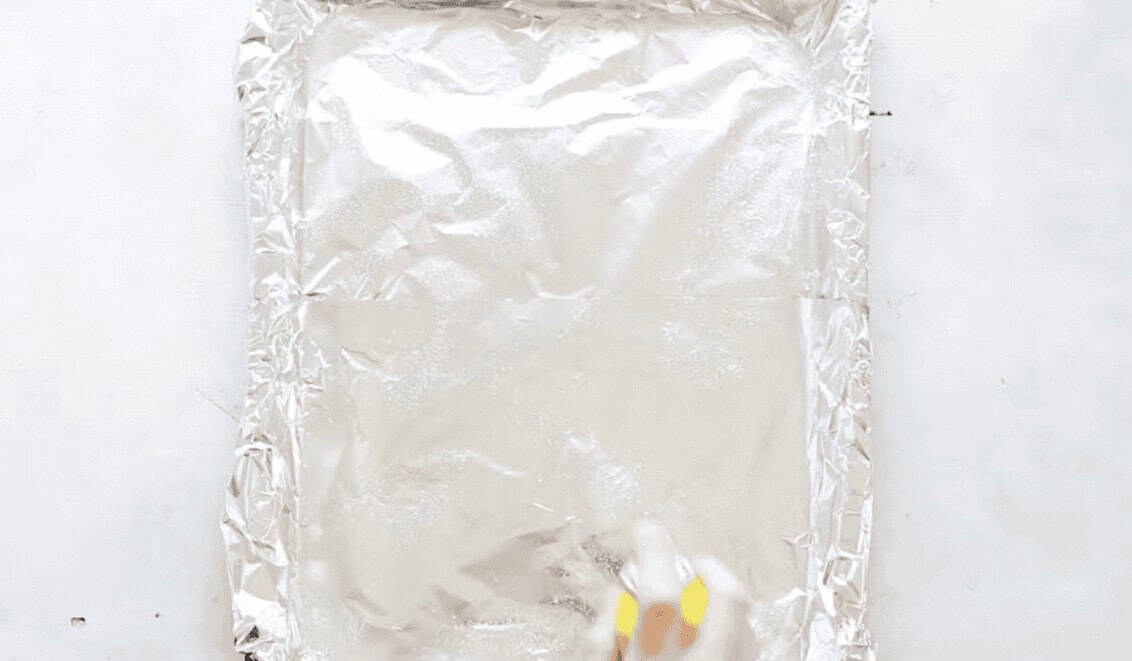 Foil covered baking sheet being sprayed with cooking spray.