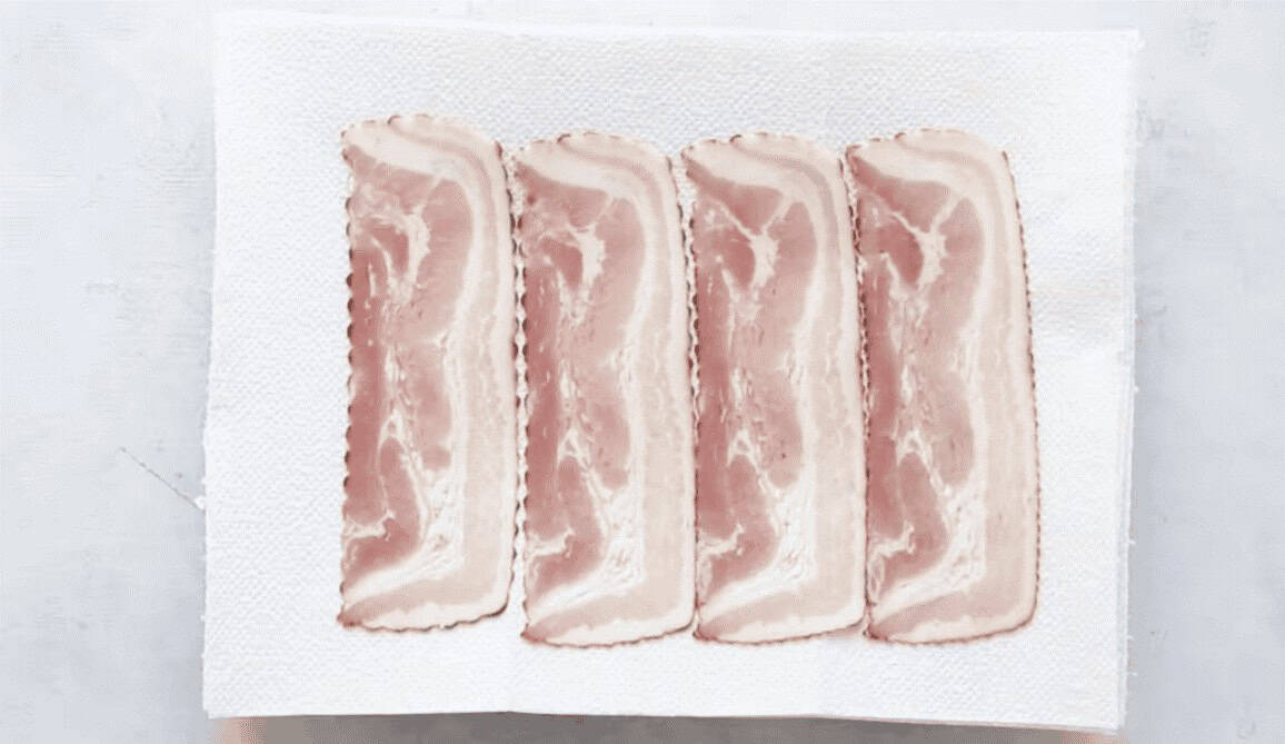 Raw bacon slices on a white cutting board.