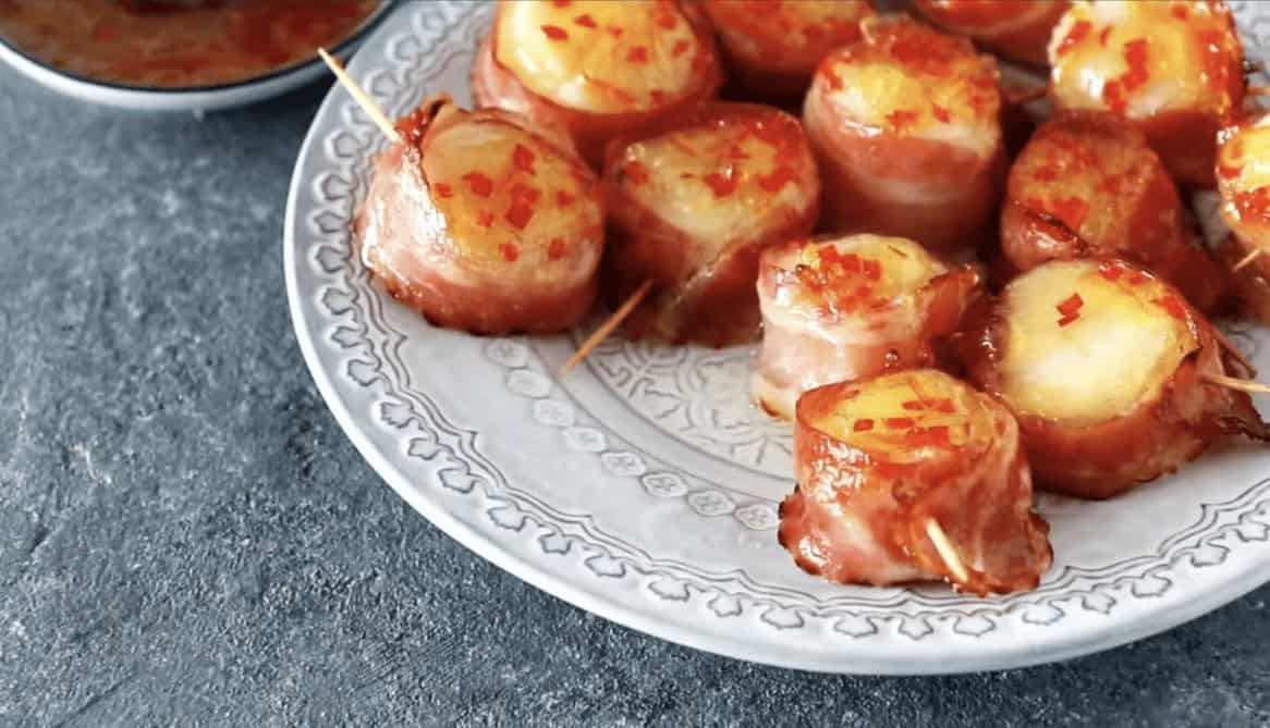 Cooked bacon wrapped scallops on a serving plate.