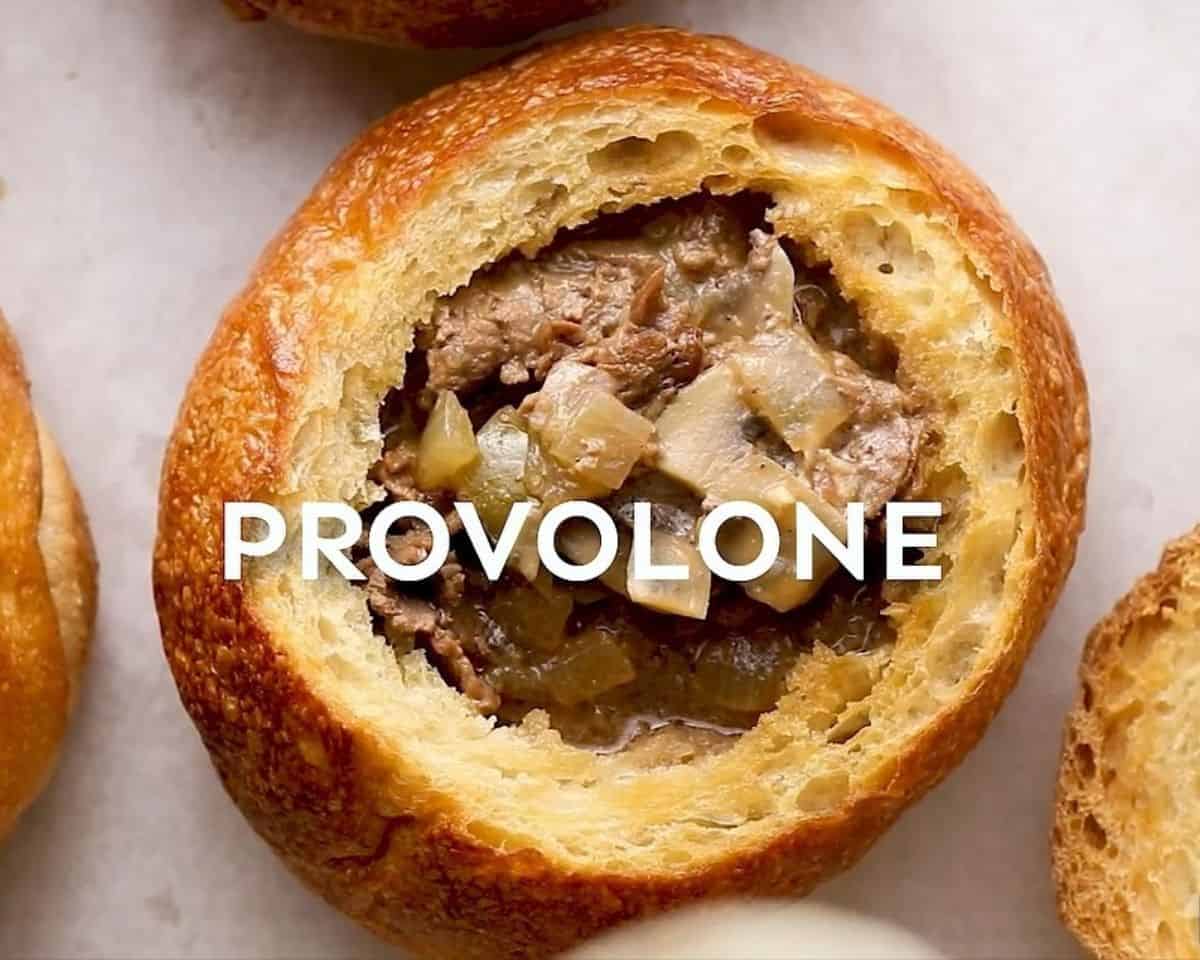 Toasted bread bowl filled with soup to be topped with provolone cheese.