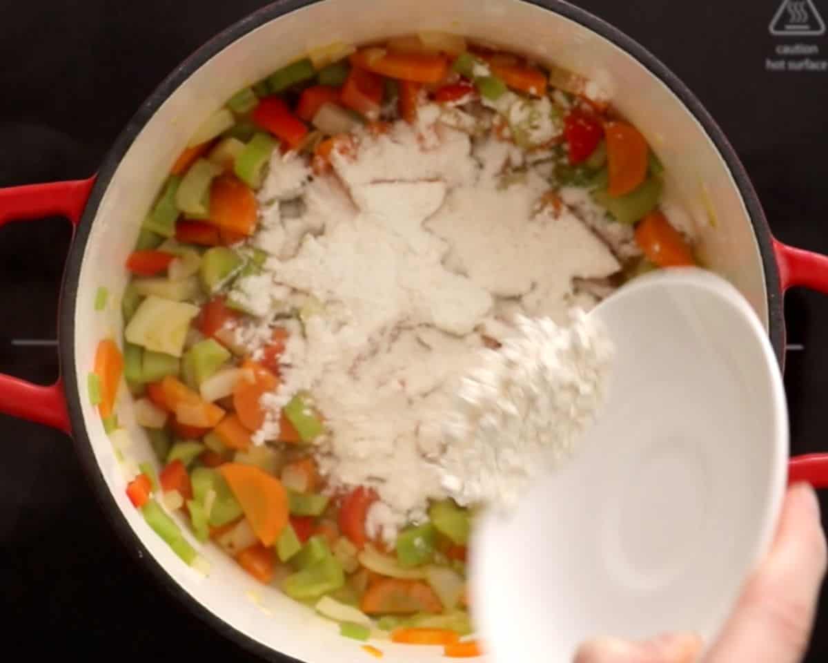 flour being added to pot with chopped onion, celery, and onions