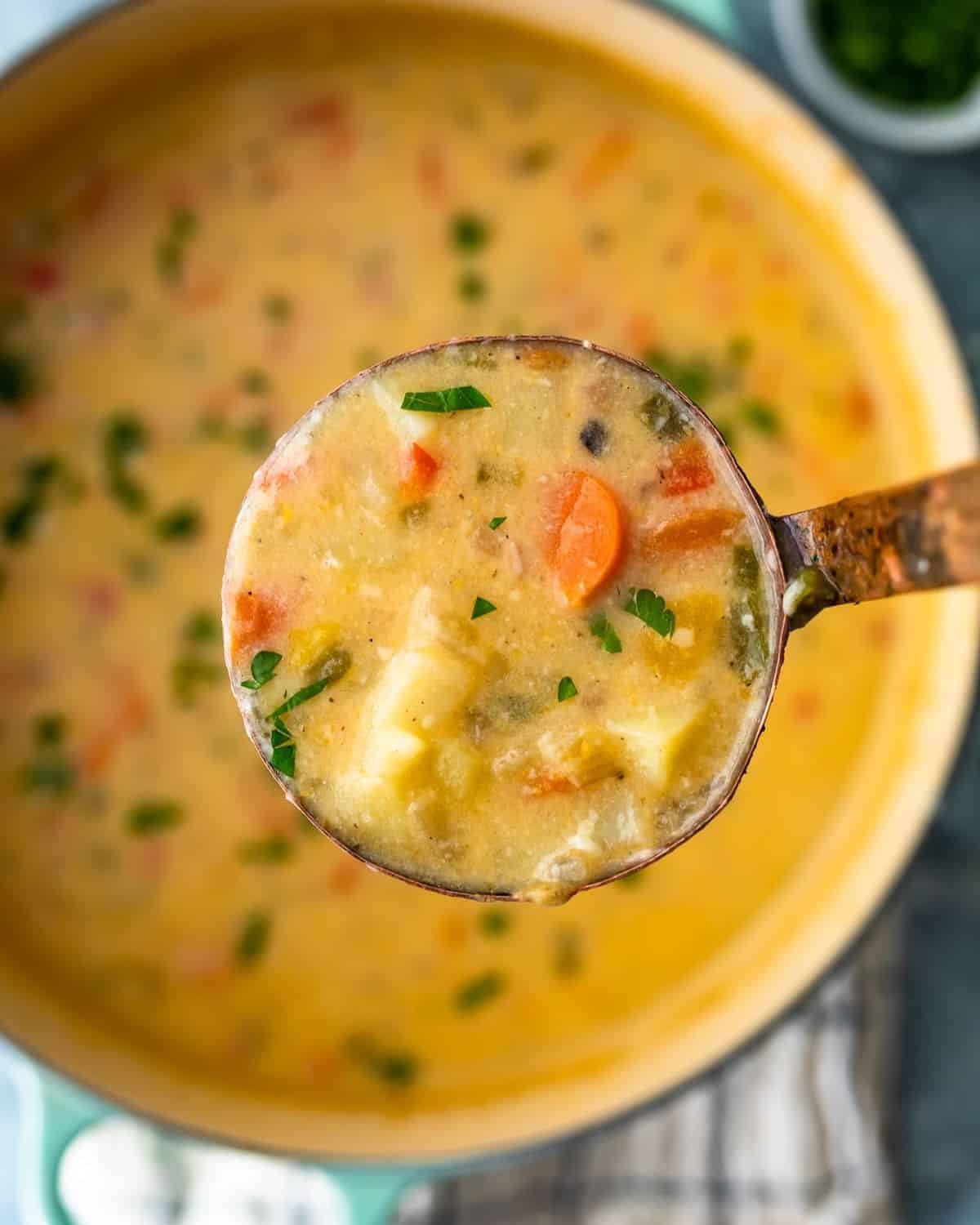 A ladle of cheesy potato soup over a pot of cheesy potato soup.
