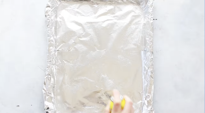 nonstick spray spraying on a foil lined baking sheet.