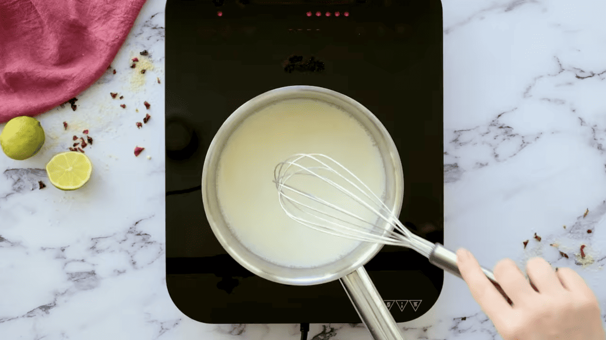 A person using a whisk to stir a bowl of pina colada sauce.