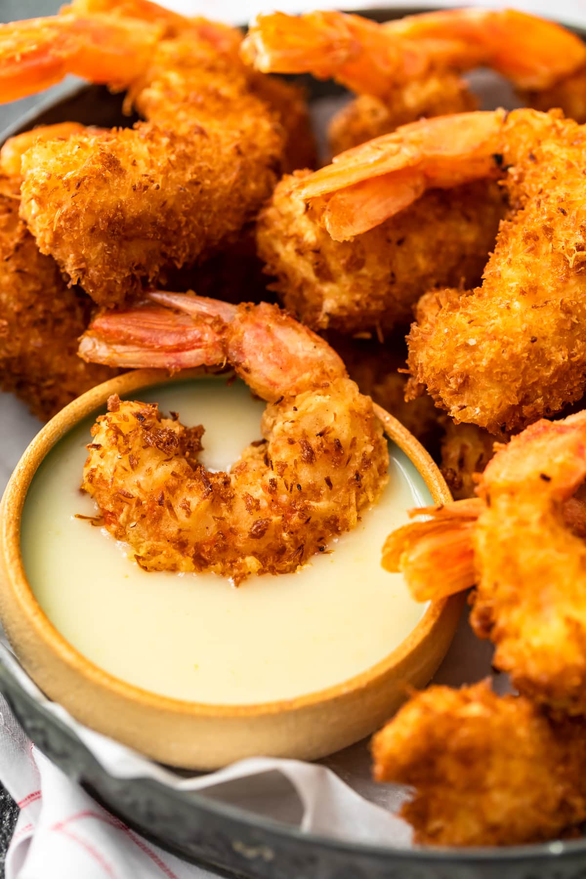 Close up on a platter of crispy coconut battered shrimp. One shrimp is dipped in a coconut sauce.