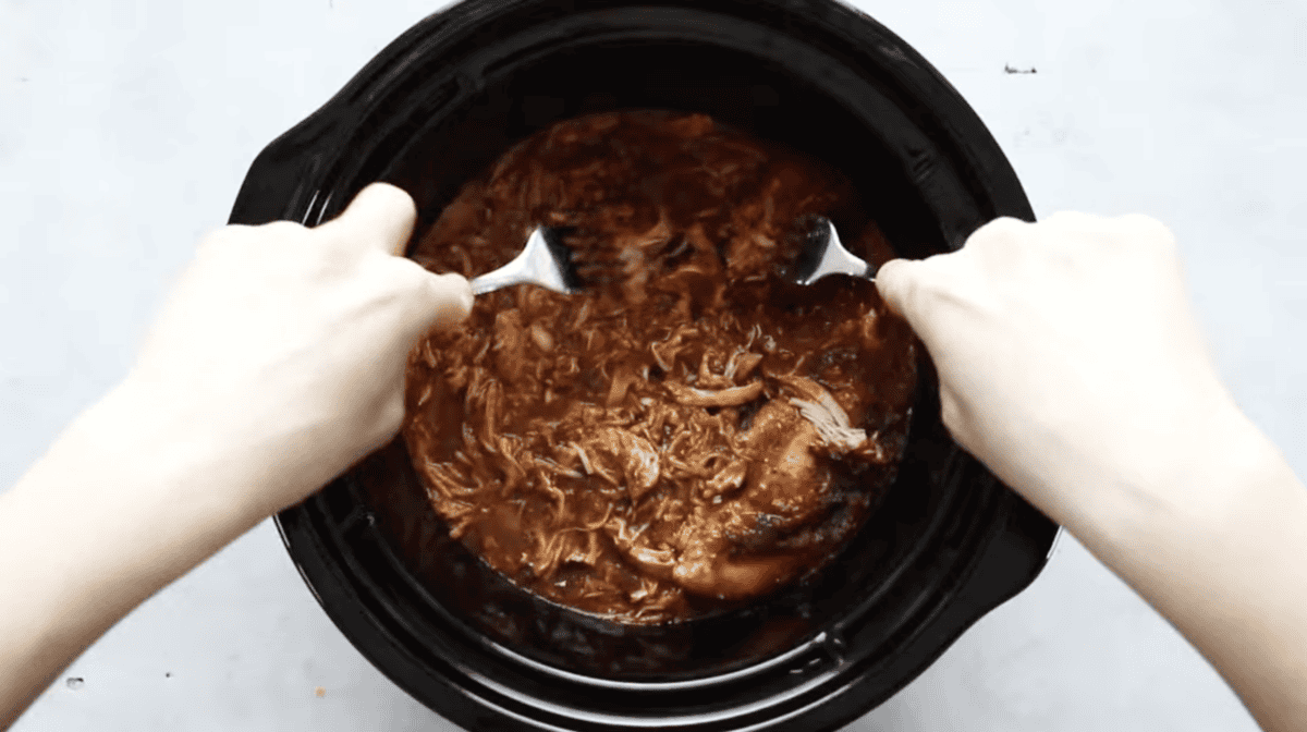 Two forks shredding chicken in a crockpot.