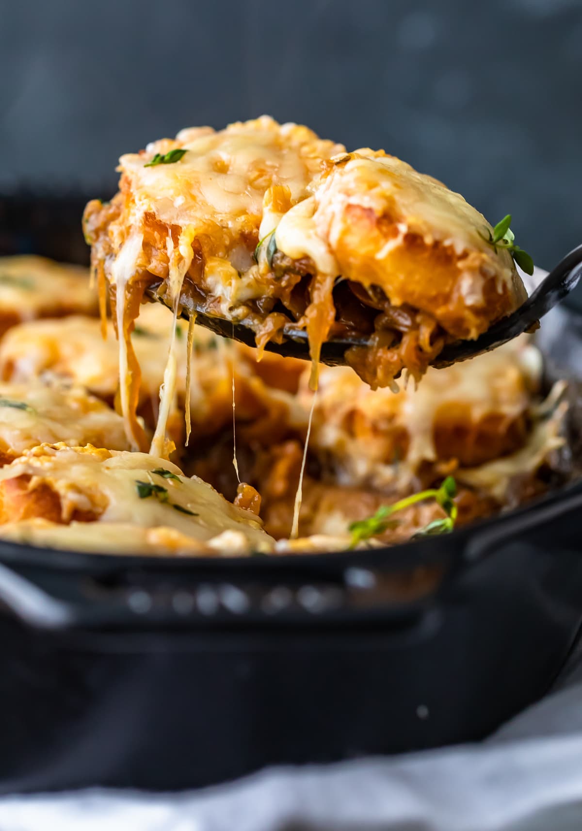 french onion soup casserole on a spoon, over a black casserole dish