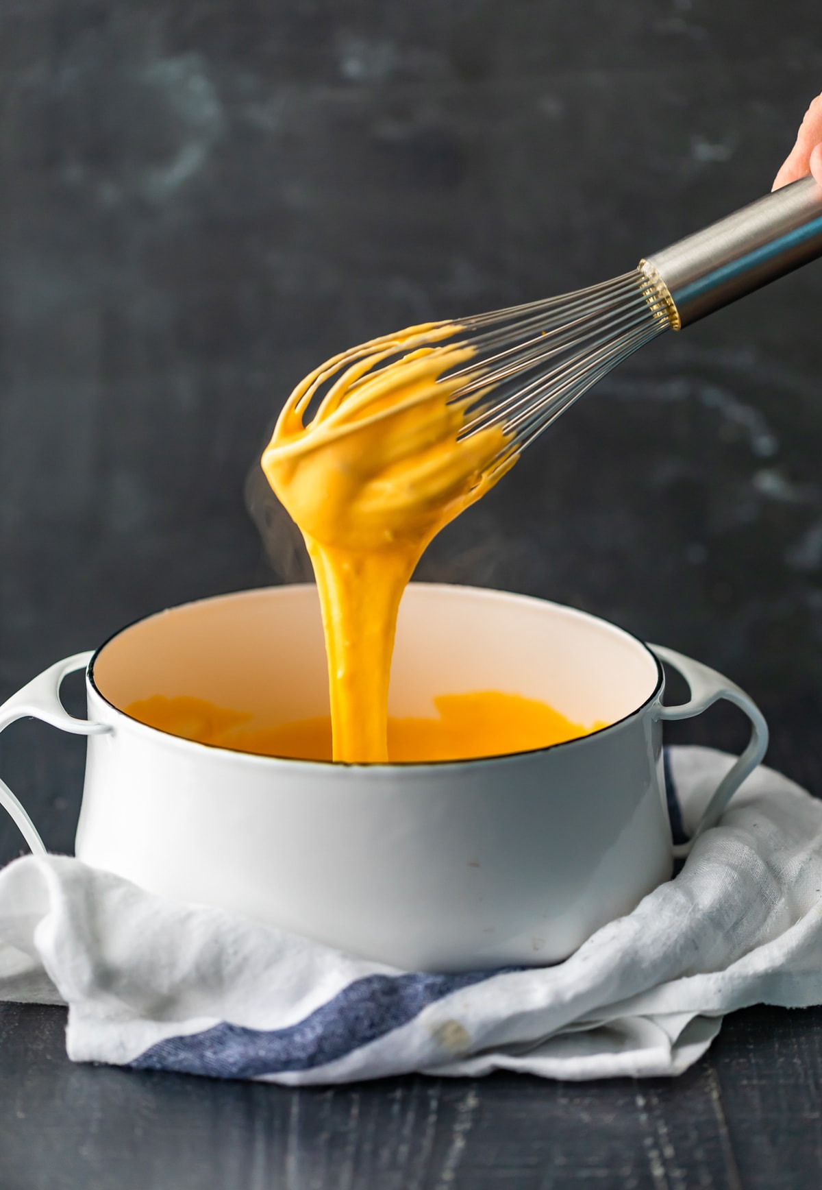 Nacho Cheese Sauce is something everyone should be able to make. An easy cheese dip (made in 5 minutes!) always comes in handy! This homemade nacho cheese sauce recipe is so delicious and so quick. Make it in a flash, dip in some chips, or use this versatile cheese sauce on all kinds of recipes! pulling a whisk out of a bowl of nacho cheese sauce