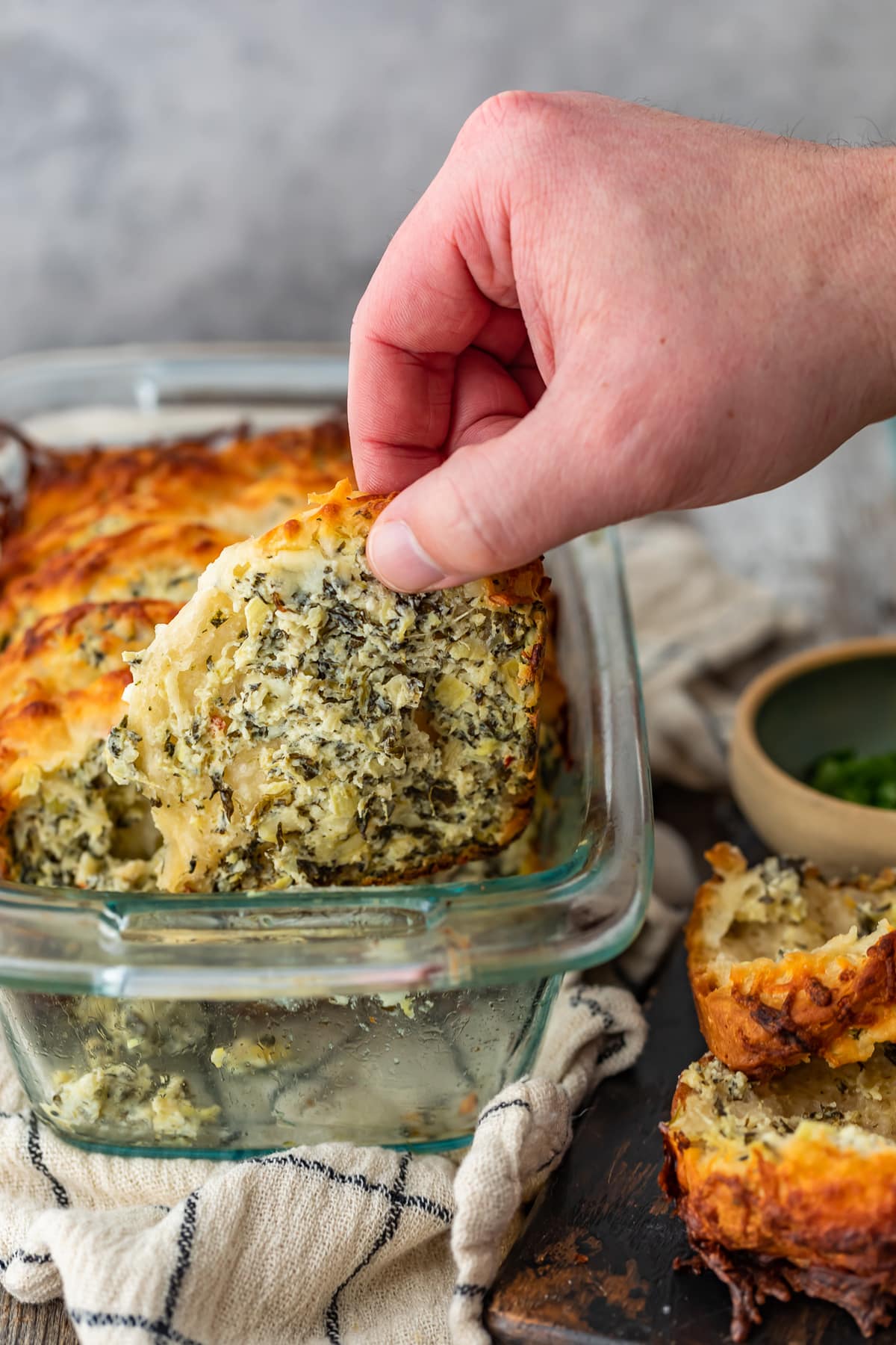 pulling a piece of spinach artichoke dip bread out of a glass loaf pan