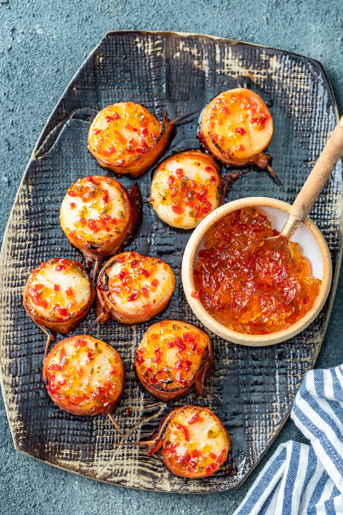 a serving platter with bacon wrapped scallops and a bowl of hot pepper jelly