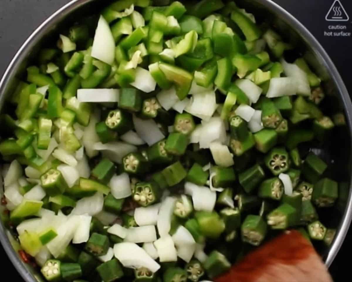 Cooking onion, green bell pepper, and okra in a pot with a wooden spoon.