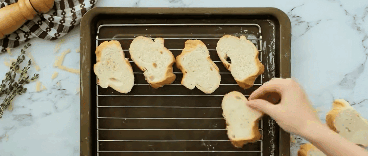 Baguette slices on a rack in an baking pan.