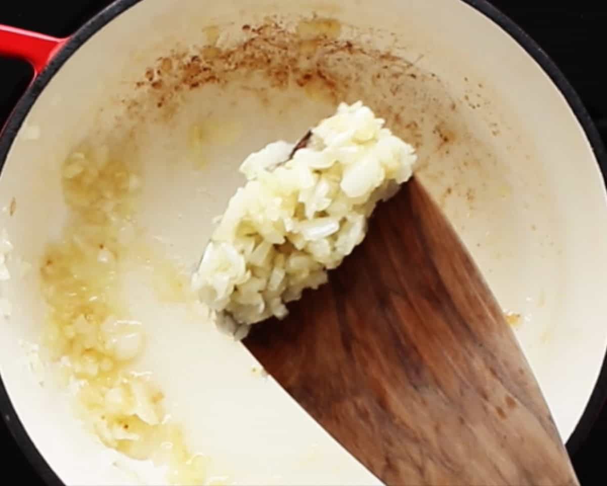 Cooking onion and garlic with a wooden a spoon.
