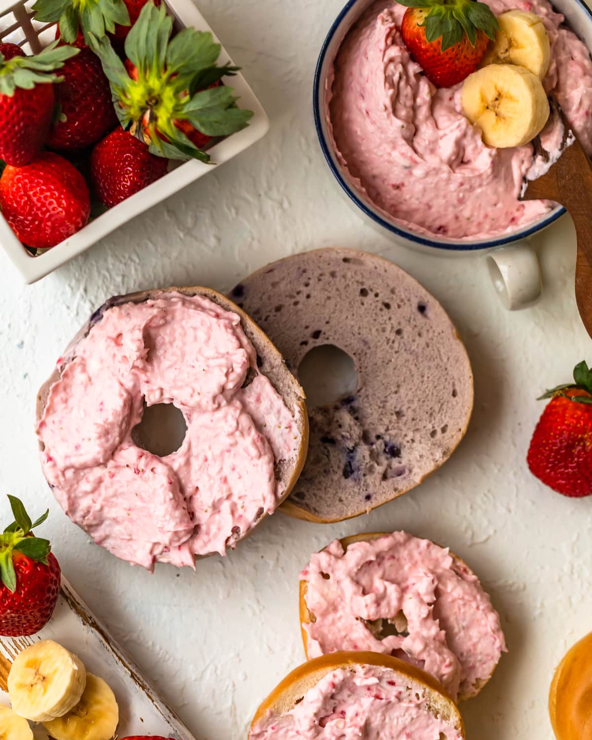 blueberry bagel with cream cheese spread, next to banana strawberry cream cheese and fresh strawberries