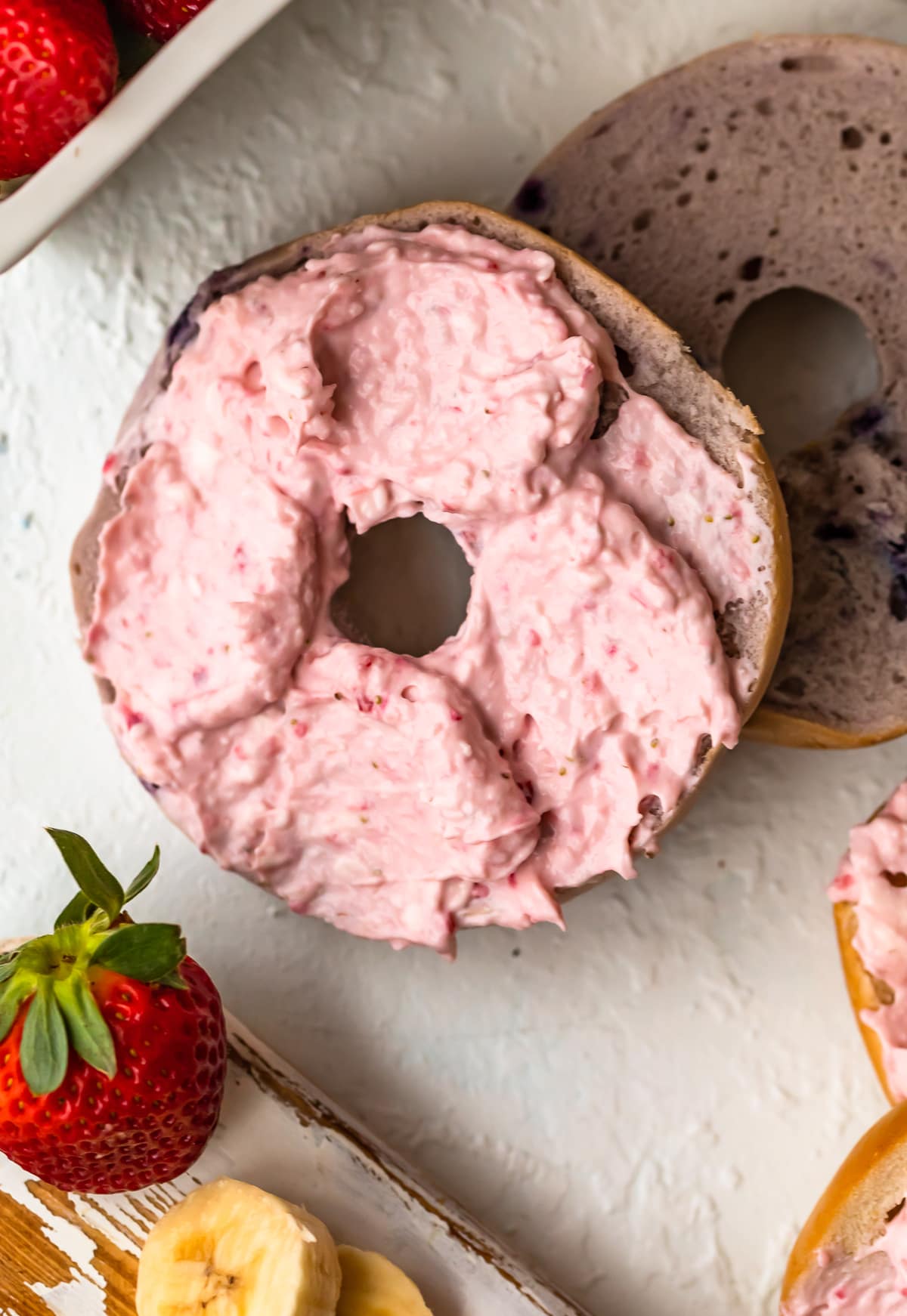 close up on a bagel topped with banana strawberry cream cheese spread