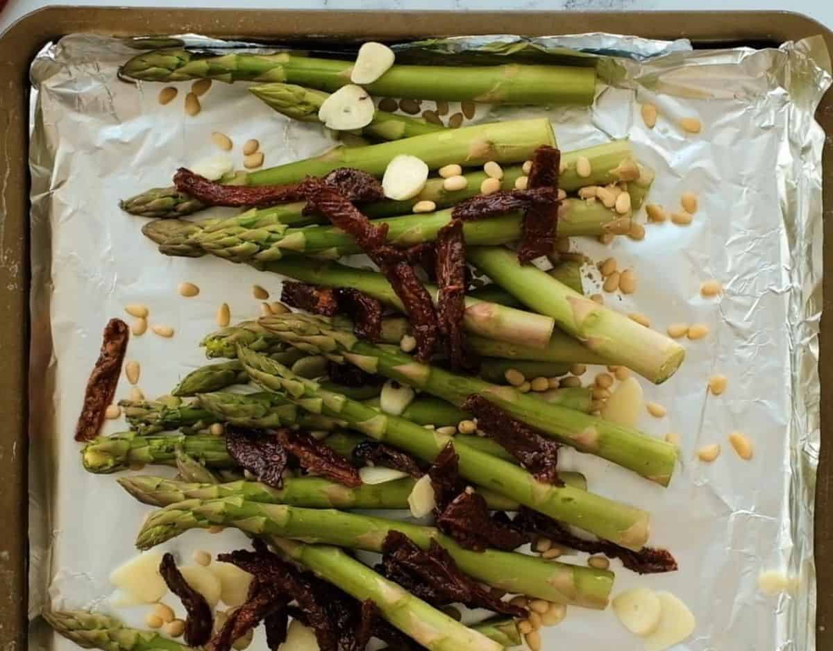 Asparagus, sundried tomatoes, pine nuts, and garlic on a foil lined baking sheet.