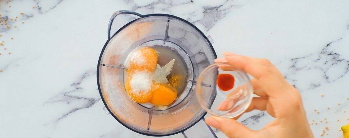 Eggs, salt, Dijon, and hot sauce being poured into a blender.
