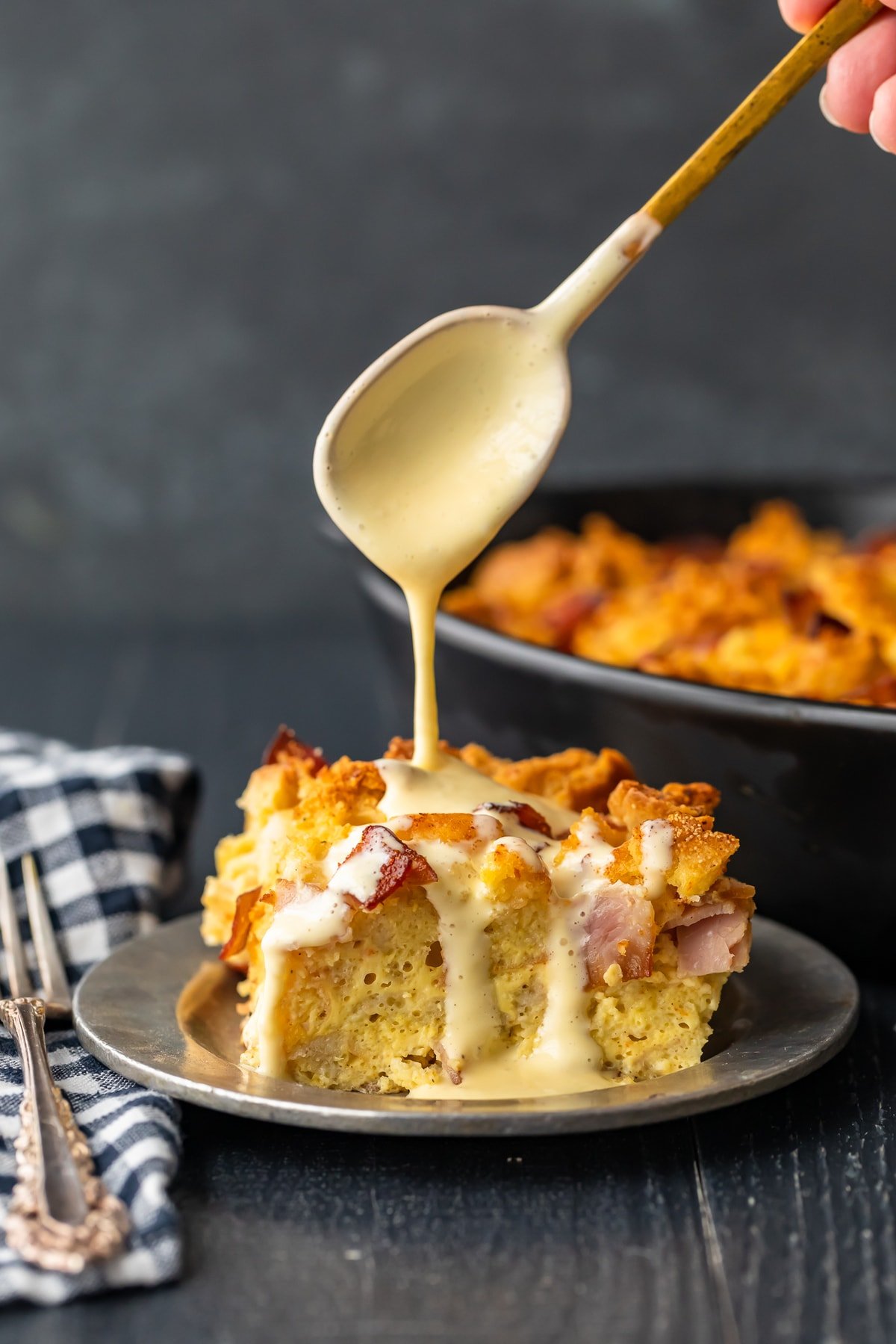 drizzling sauce over eggs benedict casserole with a spoon