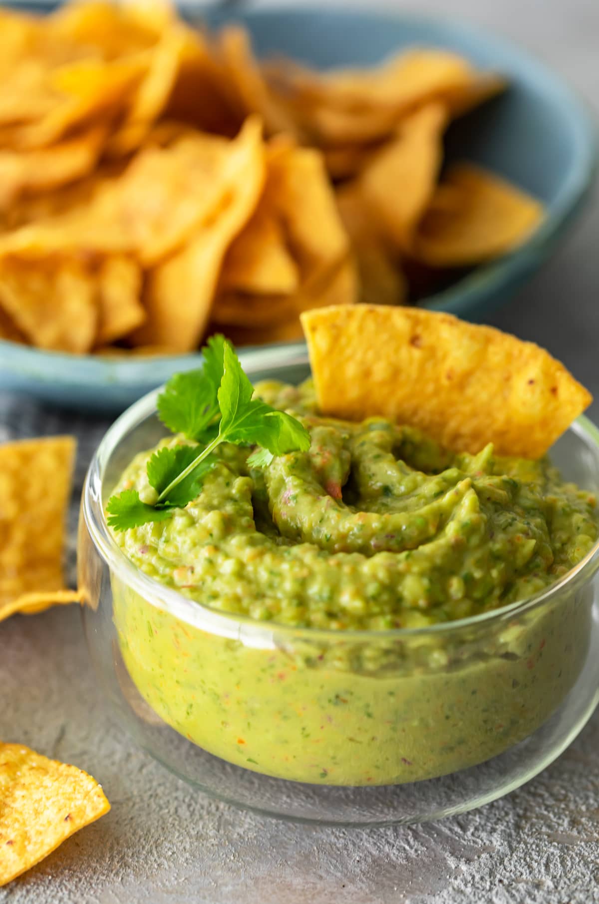 a bowl of guacamole with a chip in it in front of a bowl of chips