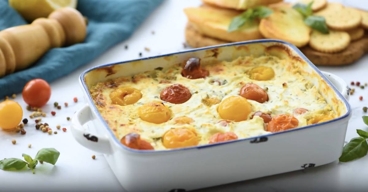 baked goat cheese dip topped with cherry tomatoes in a baking dish.