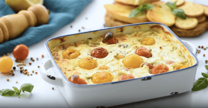 baked goat cheese dip topped with cherry tomatoes in a baking dish.