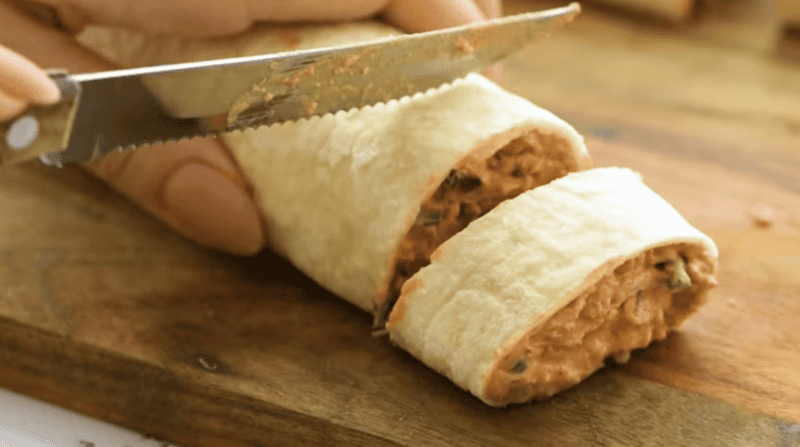 a knife slicing mexican pinwheels on a cutting board.