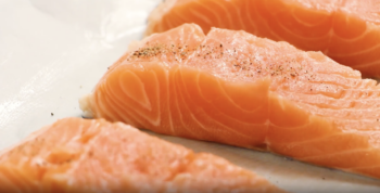 close up view of a raw salmon filet seasoned with salt and pepper on a baking sheet.