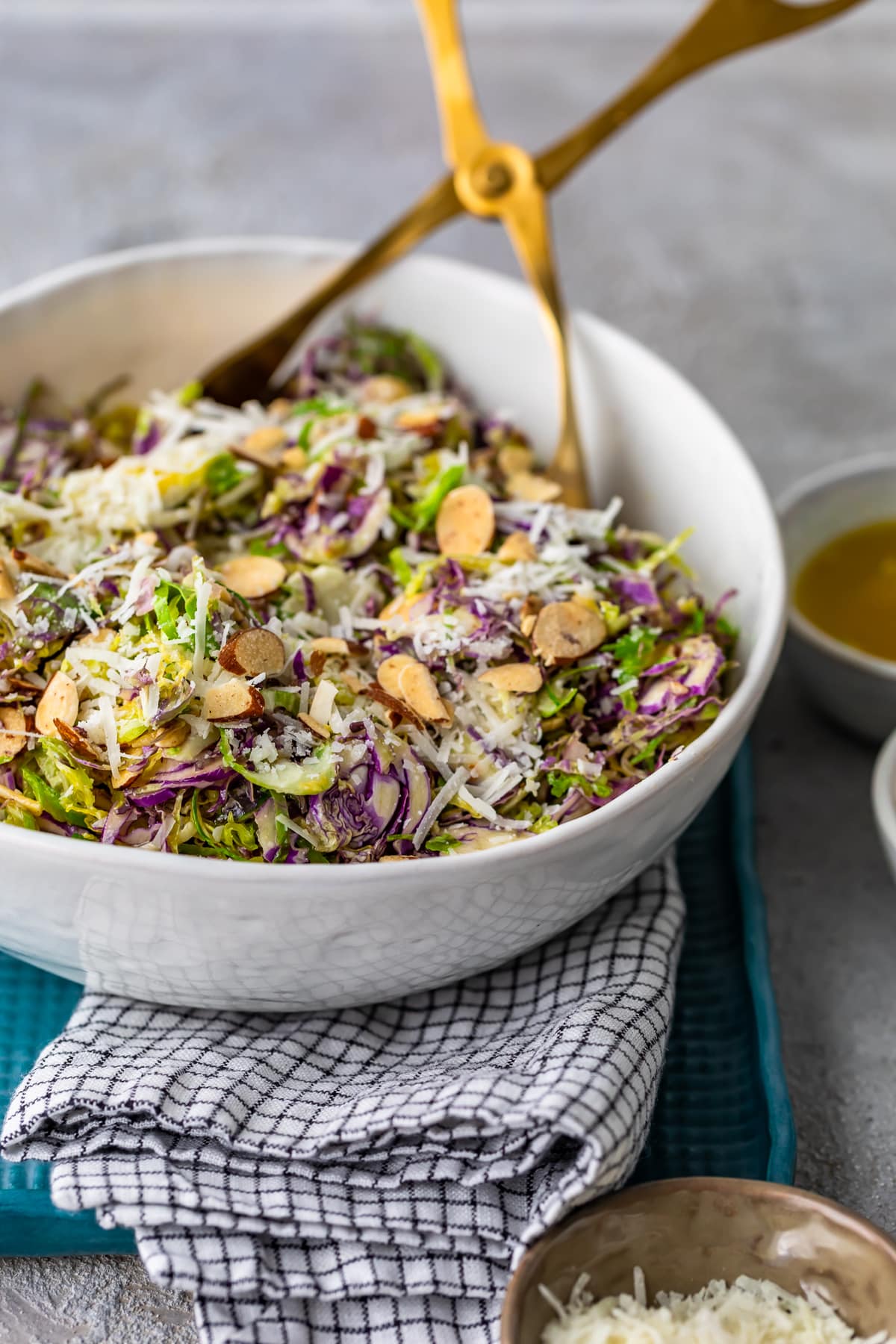 brussels sprouts salad in a white bowl with gold tongs