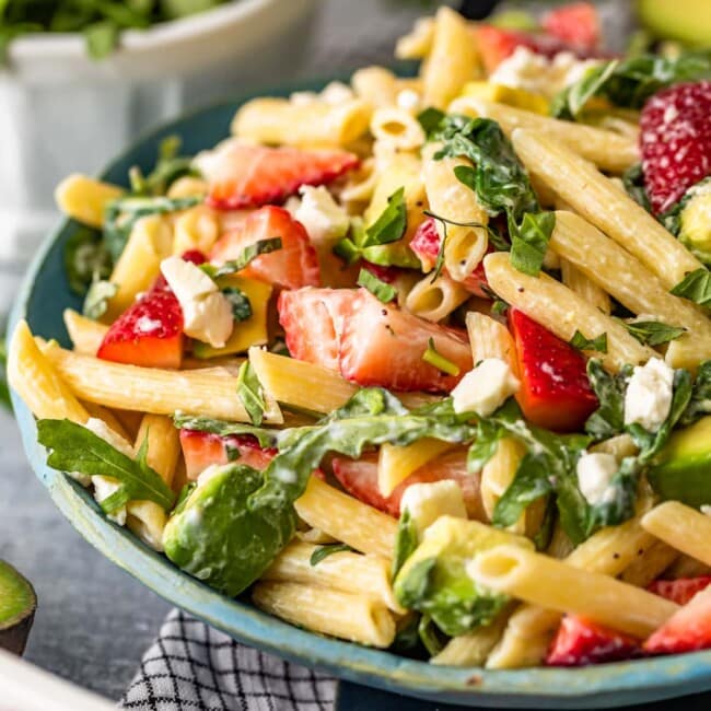 a bowl of avocado pasta salad with strawberries, spinach and feta cheese.