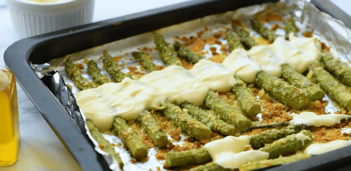 garlic asparagus with aioli drizzled on top on an aluminum lined baking sheet. 