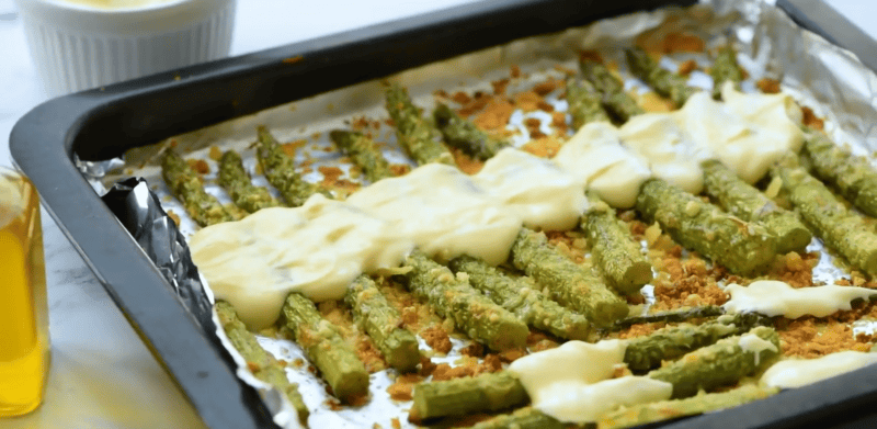 garlic roasted asparagus with aioli drizzled over it.