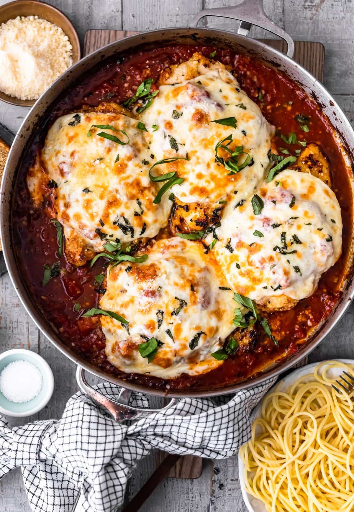 a skillet filled with marinara sauce and chicken breasts topped with cheese