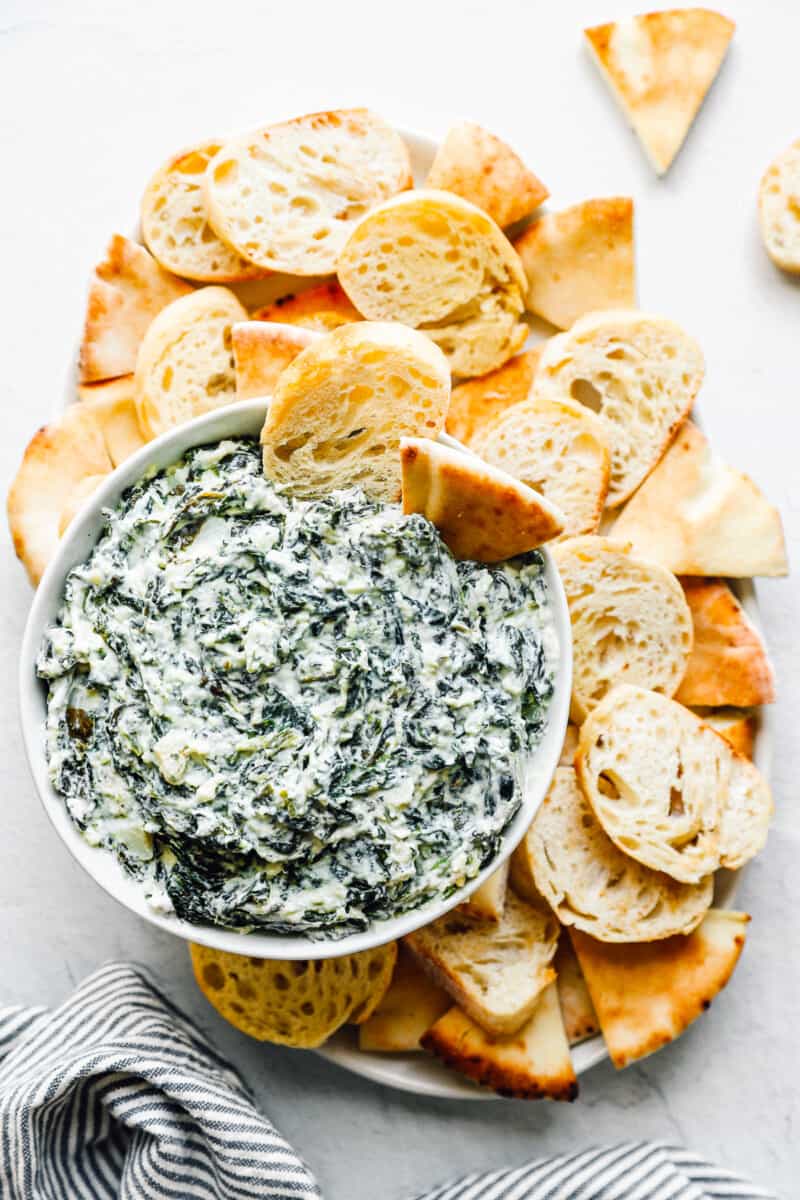 crockpot spinach dip in a white bowl with dippers
