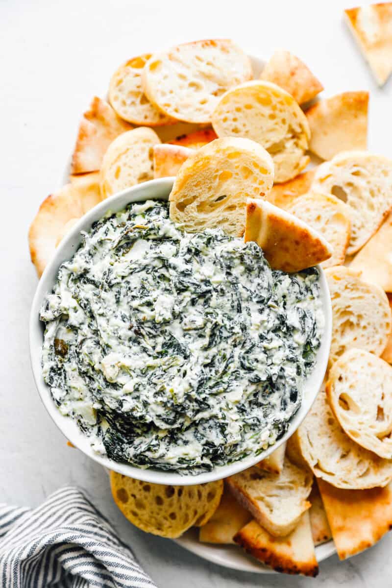 crockpot spinach dip in a white bowl with dippers