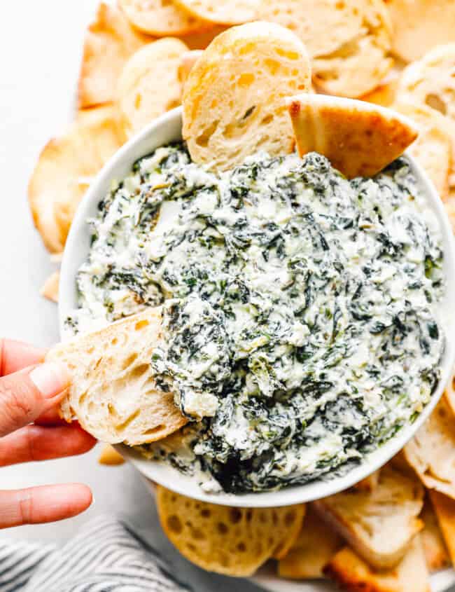 crockpot spinach dip in a white bowl with dippers